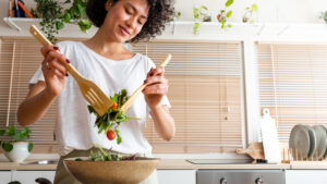 Happy young multiracial woman mixing bowl of fresh salad. Copy space.Healthy lifestyle